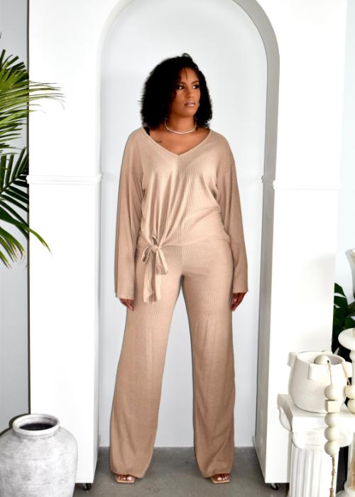 Woman wearing beige ribbed knit lounge set with tie waist, standing in archway, modern decor